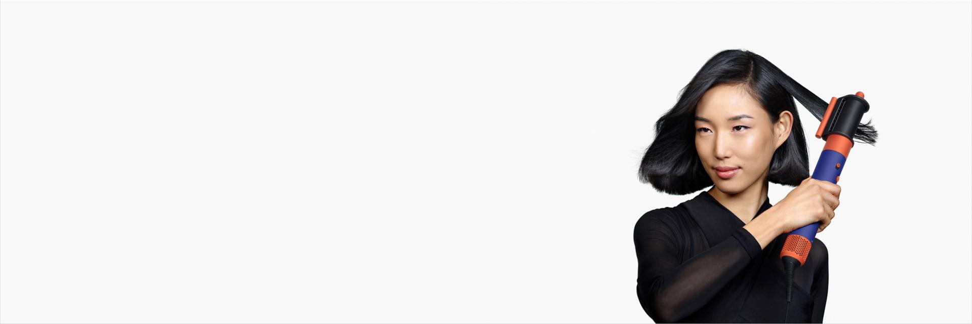 A model with medium length black hair uses the Dryer+Flyaway smoother attachment to smooth her hair style.