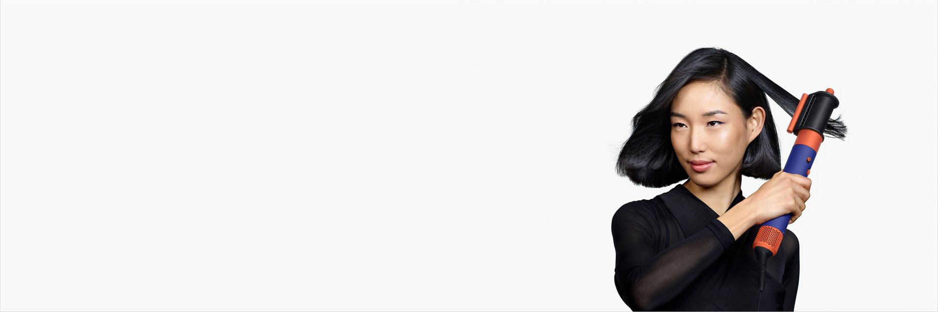 A model with medium length black hair uses the Dryer+Flyaway smoother attachment to smooth her hair style.