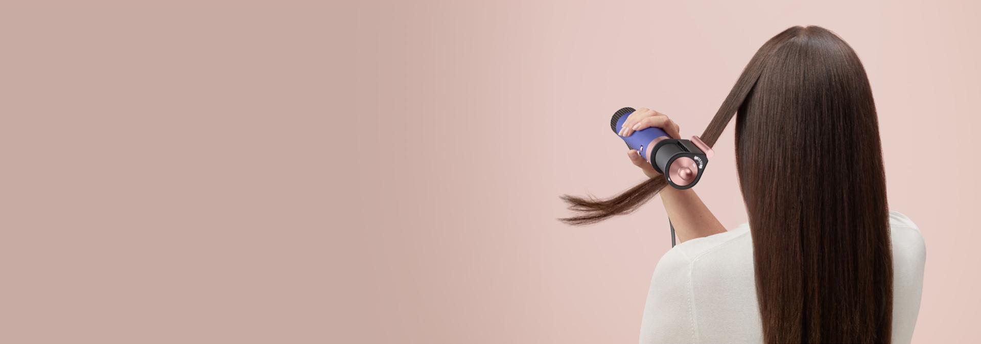 Modelka si vlasy natáčí pomocí multifunkčního stylingového přístroje a fénu Dyson Airwrap Origin.