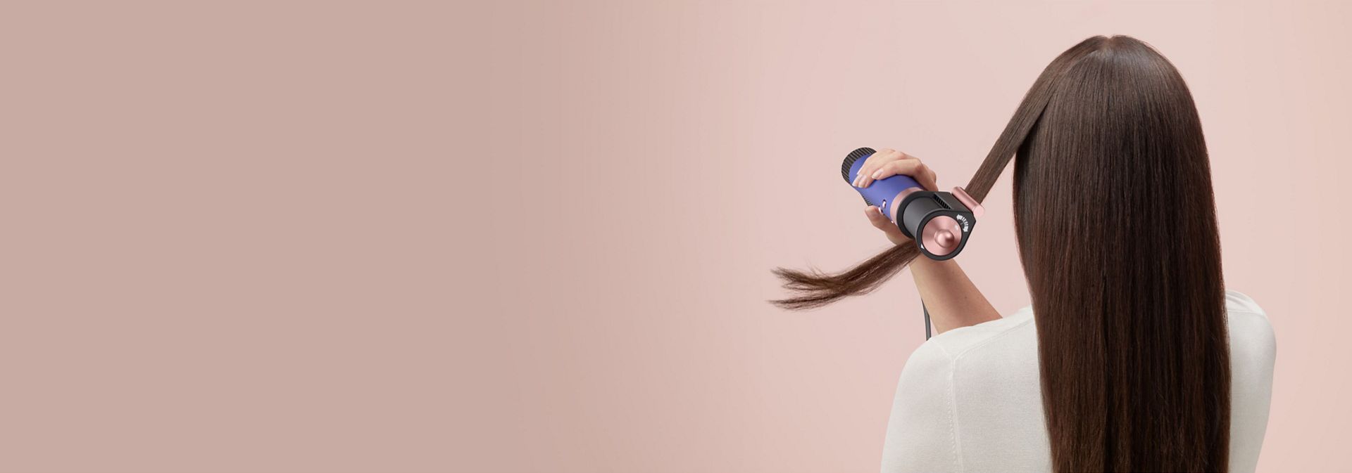Modelka si vlasy natáčí pomocí multifunkčního stylingového přístroje a fénu Dyson Airwrap Origin.
