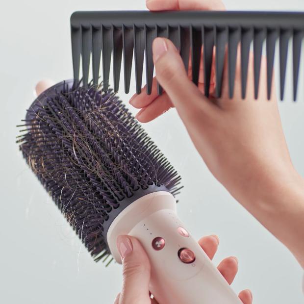 Hair is cleared from the bristles of the Dyson Airsmooth styling brush using a comb.