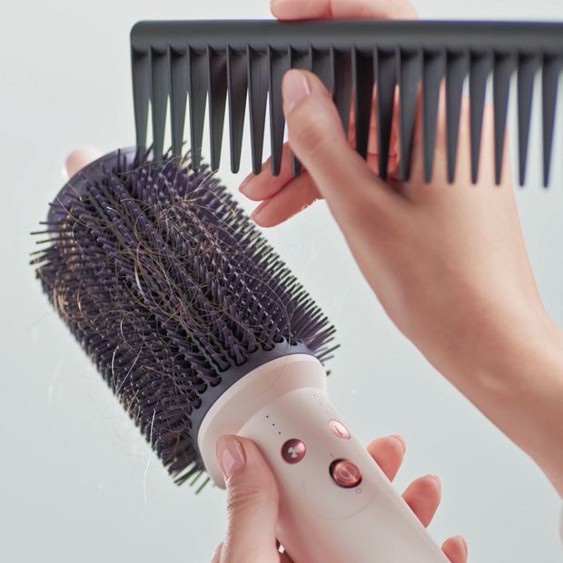 Hair is cleared from the bristles of the Dyson Airsmooth styling brush using a comb.