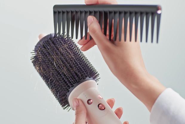 A comb is used to clean tangled hair from the Dyson Airsmooth styling brush bristles.