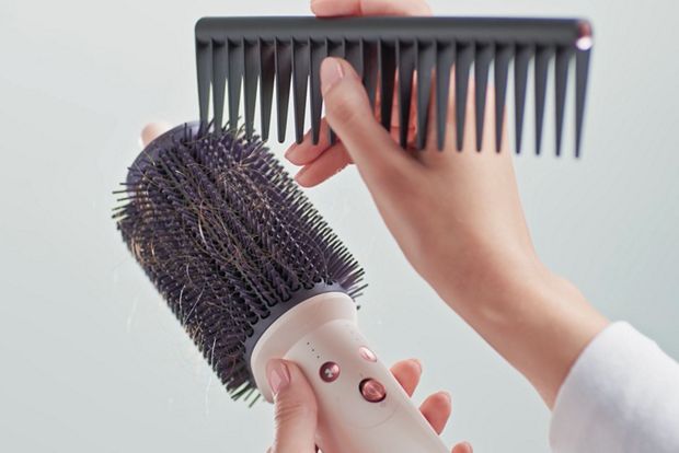 A comb is used to clean tangled hair from the Dyson Airsmooth styling brush bristles.