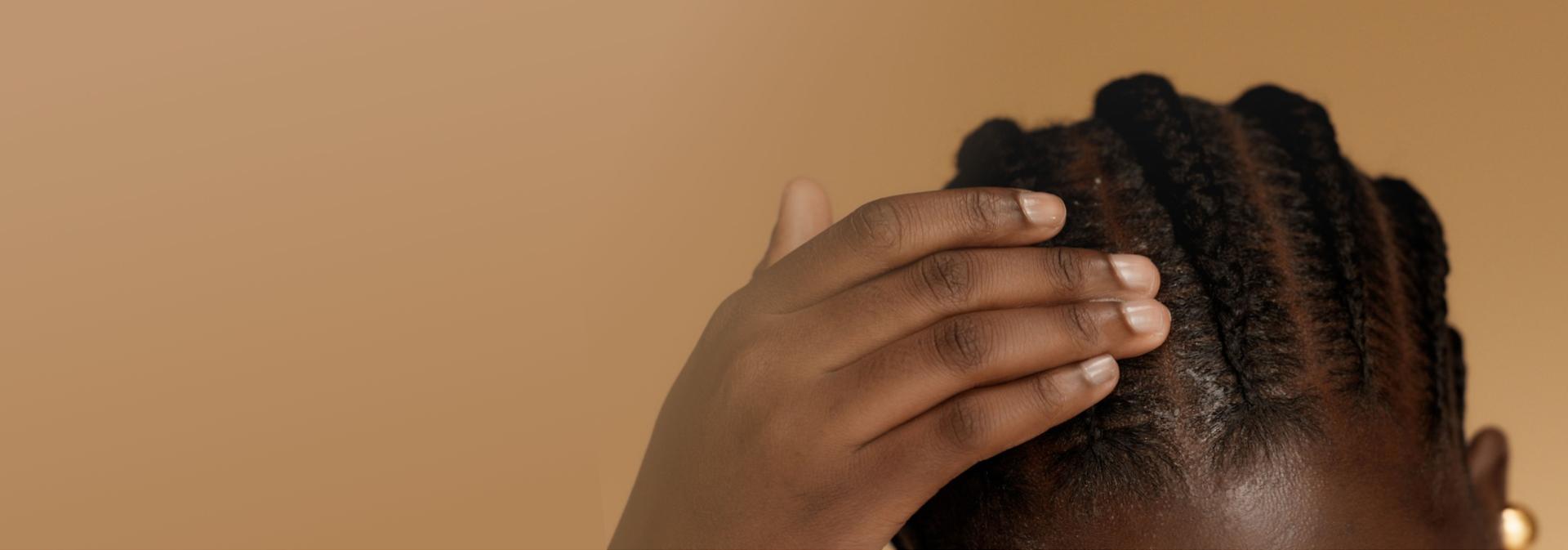 A model with coily hair styled into braids touches their scalp.
