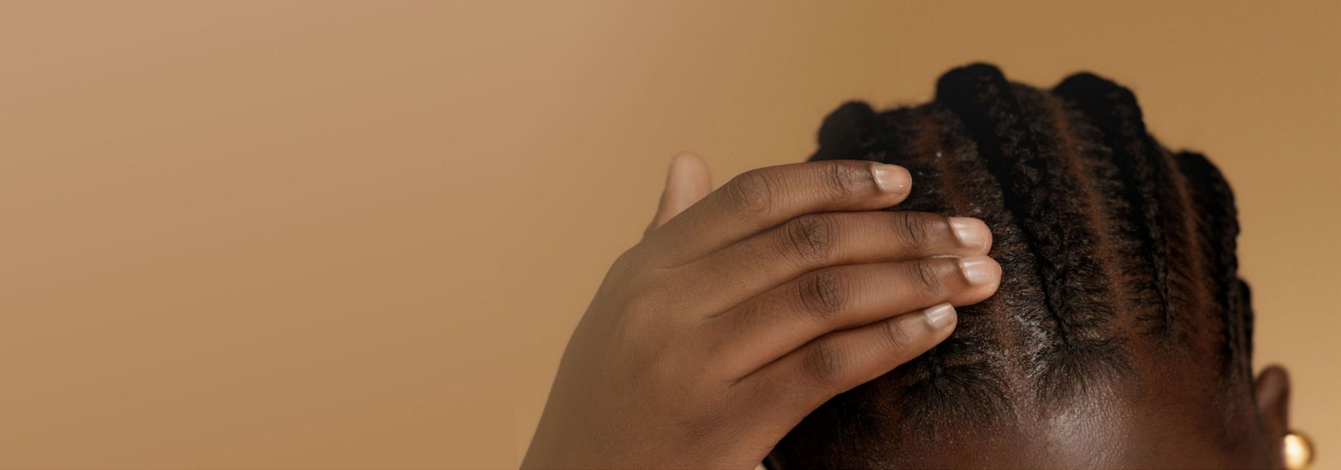 A model with coily hair styled into braids touches their scalp.