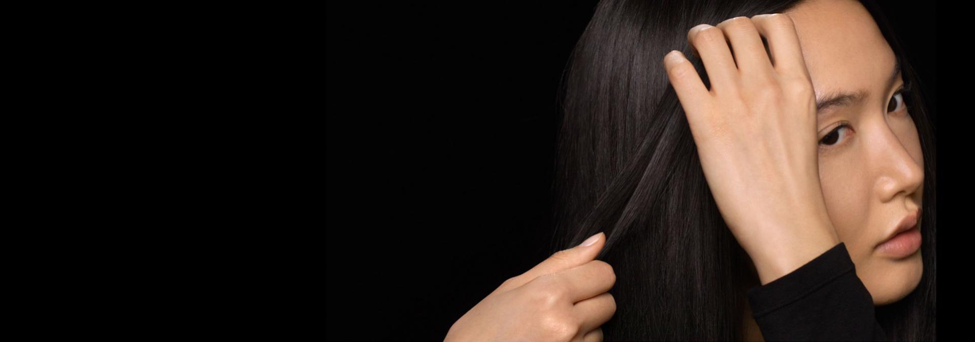 Tmavovlasá modelka si na vlasy nanáší post-stylingové sérum Dyson Chitosan.