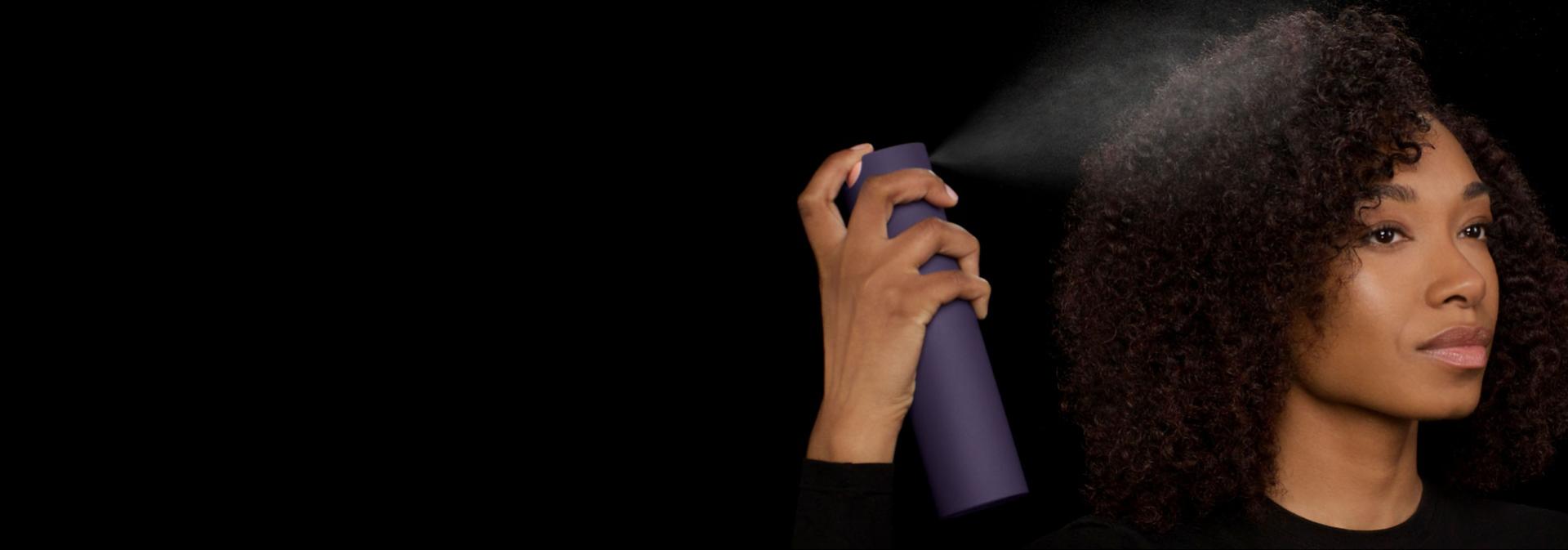 Modelka s kudrnatými vlasy nanáší na své vlasy multifunkční stylingový sprej Dyson Chitosan.