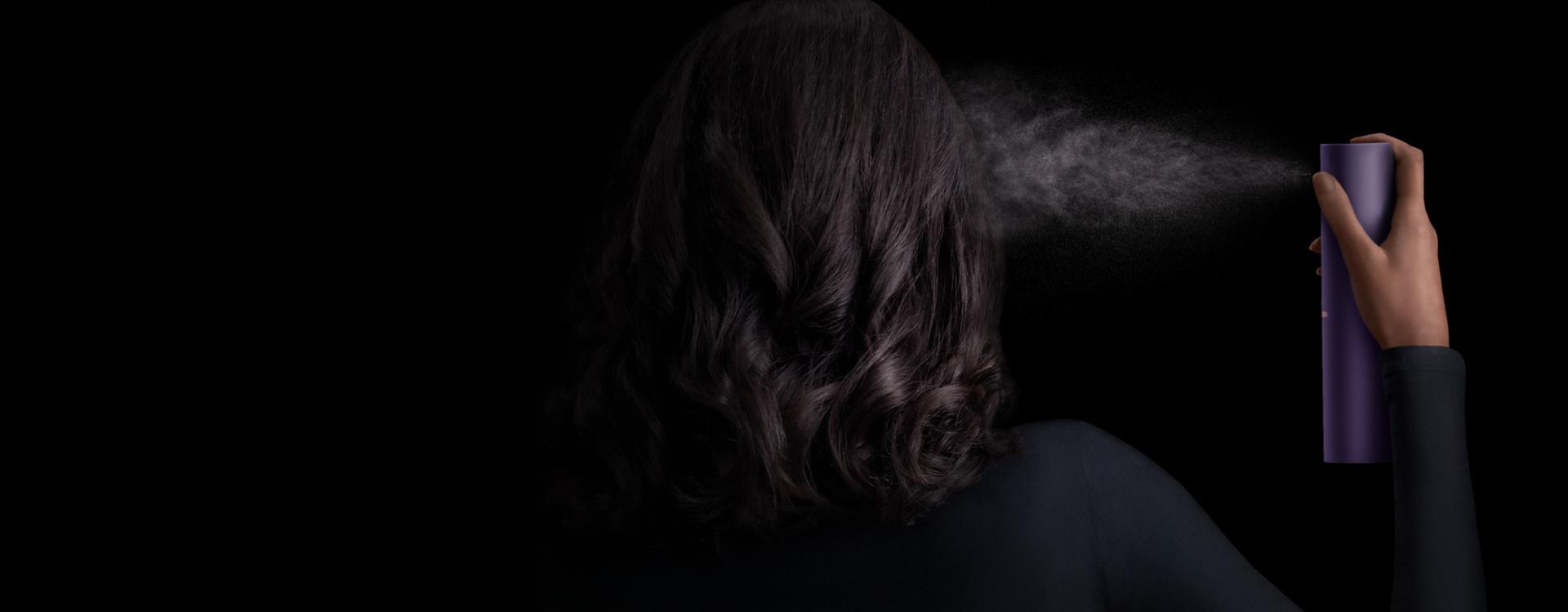 Model with dark hair applies Dyson Chitosan Multi-use styling spray to her hair.