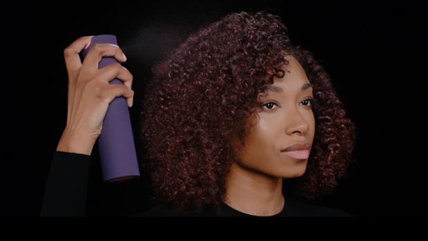 A model sprays her styled hair with Dyson Chitosan Multi-use styling spray to revive the style.