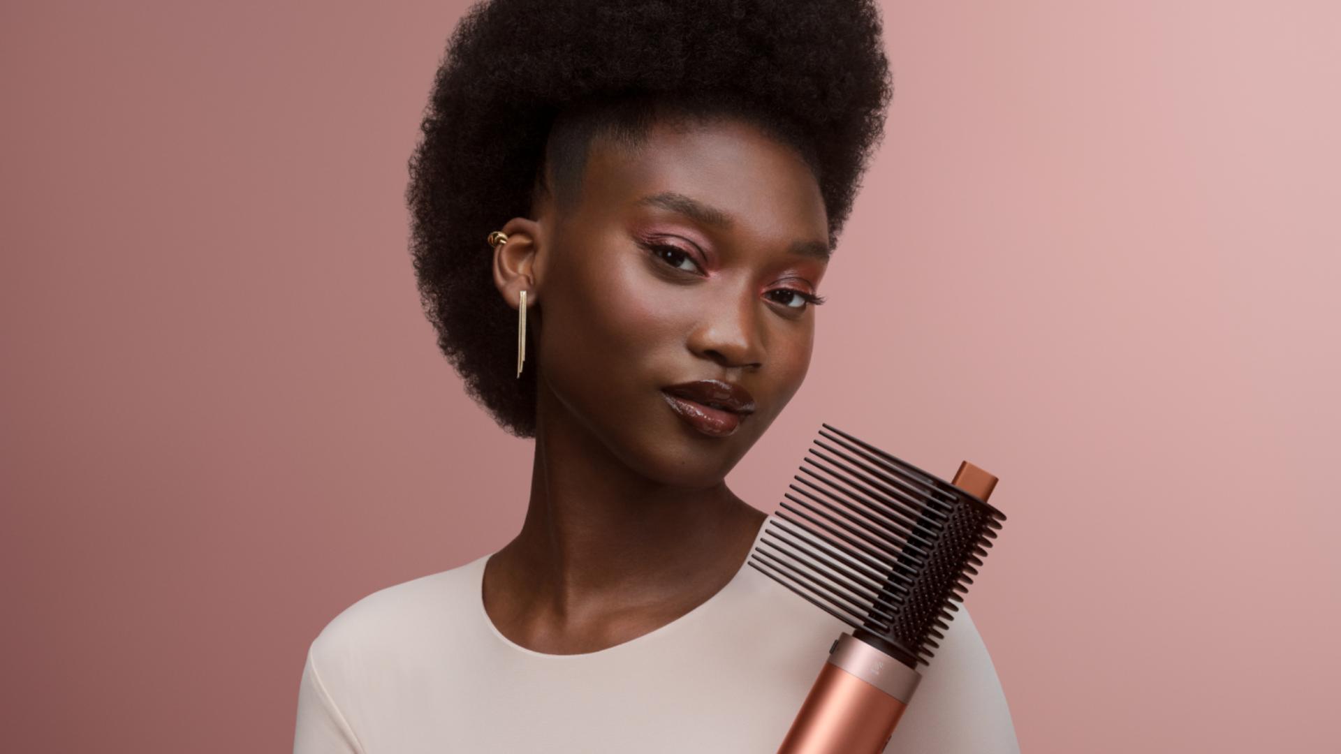 Modelka drží multistyler a vysoušeč Dyson Airwrap Co-anda2x s narovnávacím hřebenem 2x.