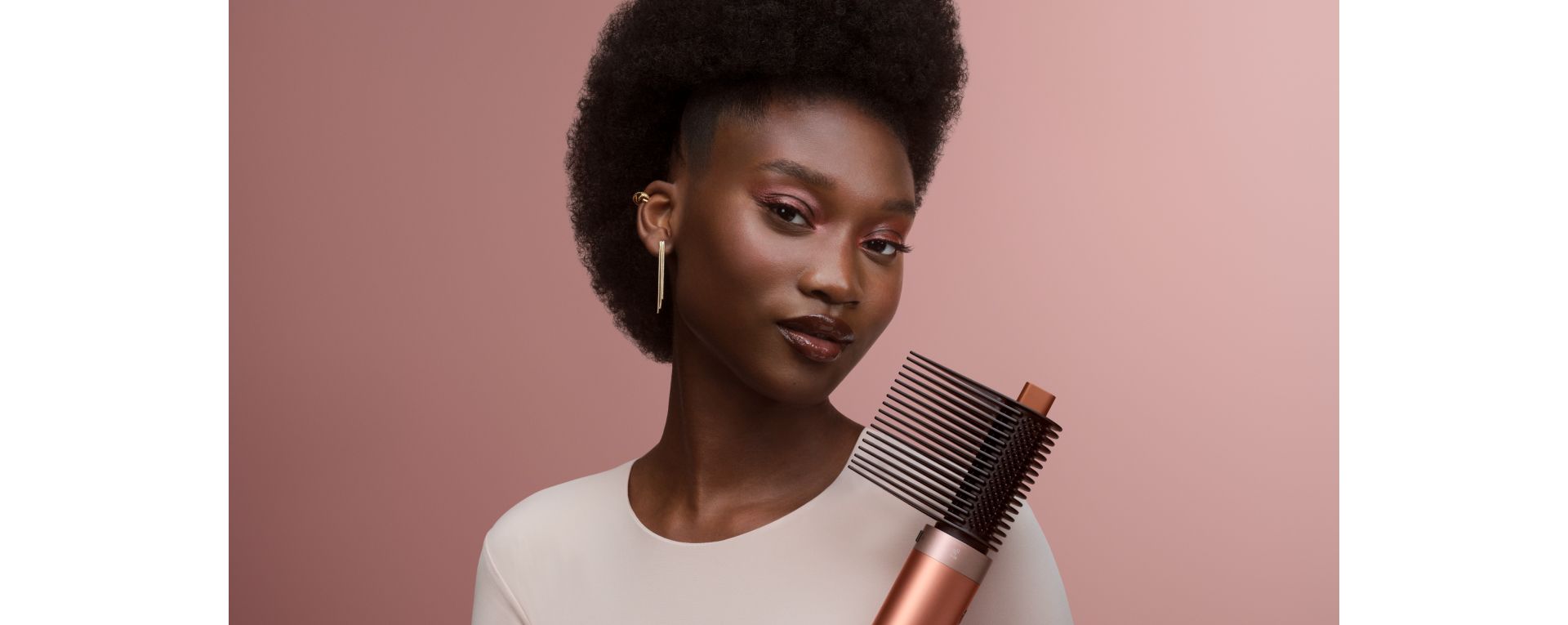 A model holds the Dyson Airwrap Co-anda2x multi-styler and dryer with the Tension comb 2x attachment.