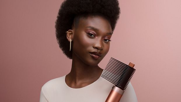 A model holds the Dyson Airwrap Co-anda2x multi-styler and dryer with the Tension comb 2x attachment.