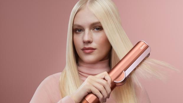 A blonde model dries and styles her hair with the Dyson Airstrait dryer and straightener.