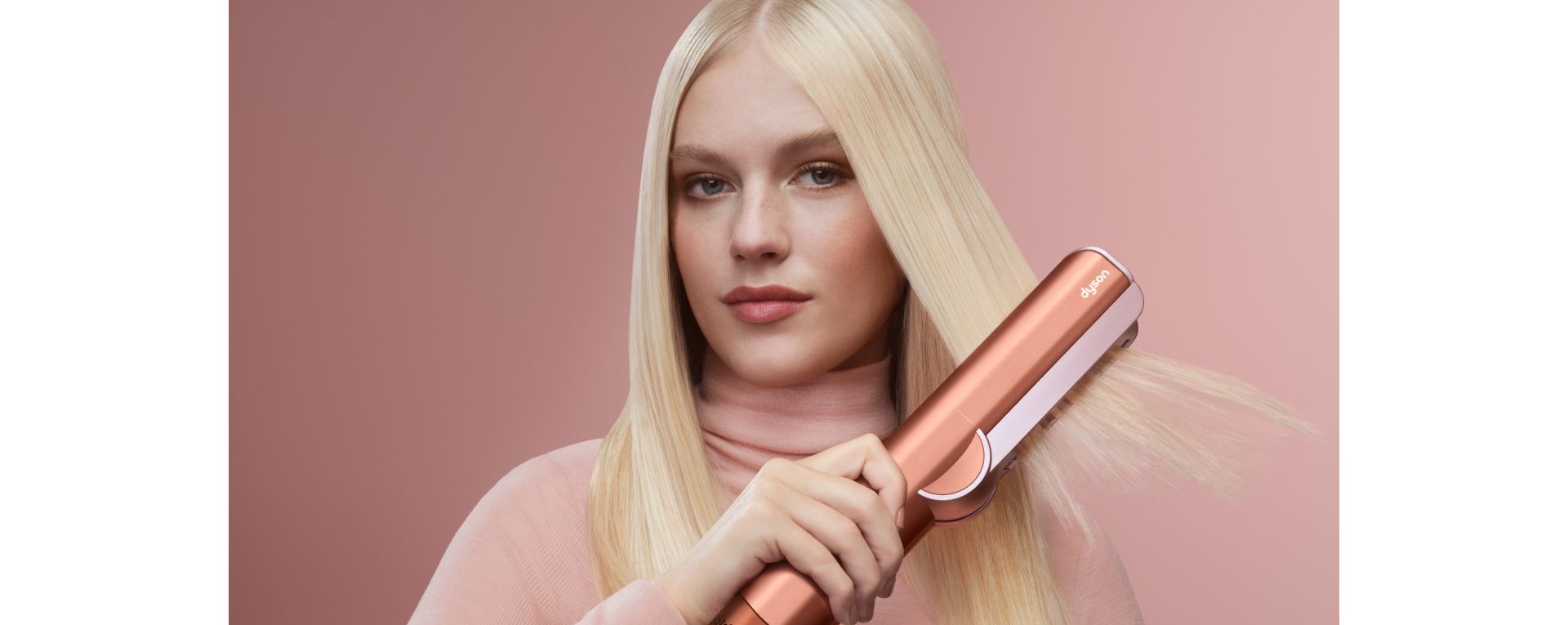 A blonde model dries and styles her hair with the Dyson Airstrait dryer and straightener.