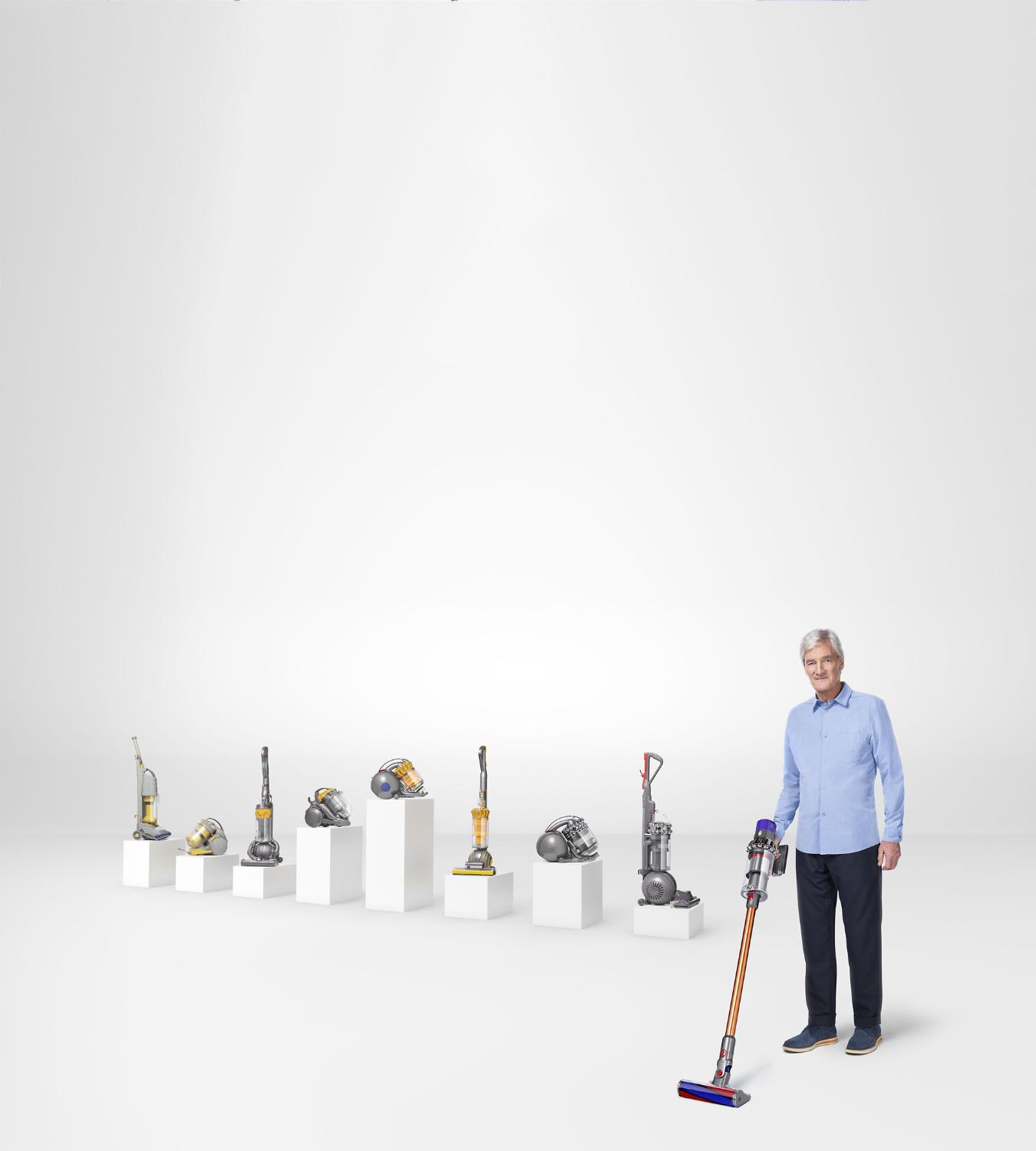 James Dyson using a Dyson Cyclone V10™ vacuum in front of old Dyson machines on plinths.