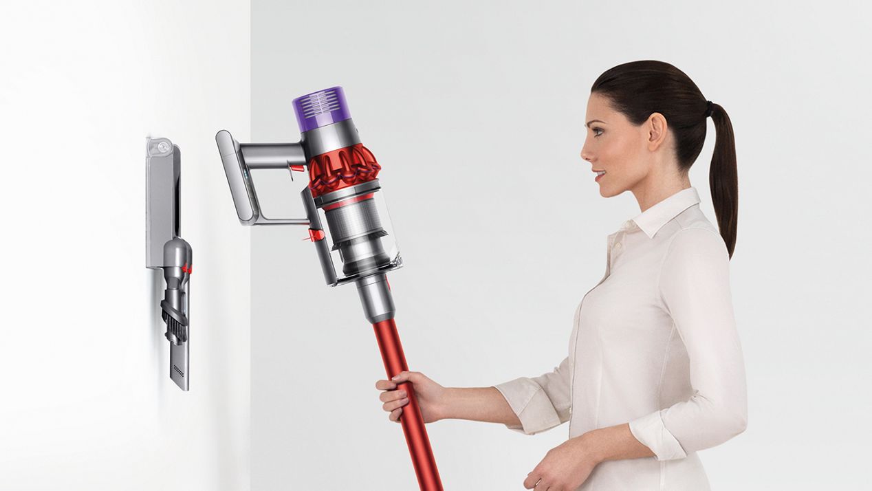 dyson-cyclone-v10-vacuum-wall-mounted-dock Donna che ripone ordinatamente Dyson Cyclone V10 nella stazione di ricarica