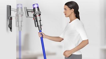 Woman placing Dyson V11™ cordless vacuum cleaner into wall charging dock