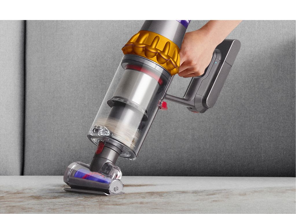 Dyson V15s with Hair screw tool in handheld mode removes fur from a sofa while a cat sits nearby.