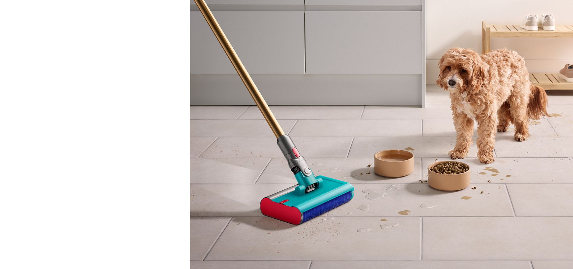Dog stares past food and water bowl as Dyson Submarine wet roller head cleans up crumbs and spilt water across the kitchen floor.