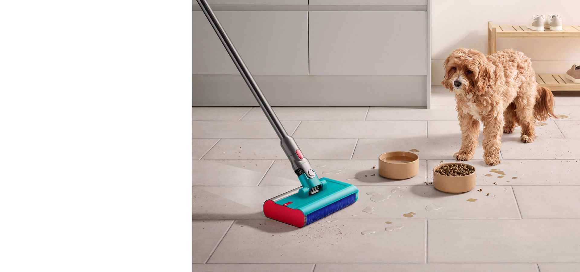 Dog stares past food and water bowl as Dyson Submarine wet roller head cleans up crumbs and spilt water across the kitchen floor.
