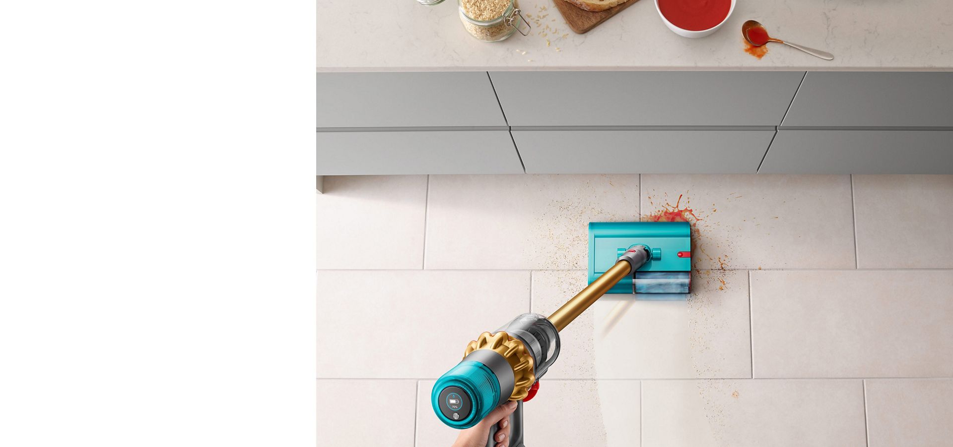 Dyson V15s Detect Submarine wet roller head clearing up spilt soup and breadcrumbs on a tiled kitchen floor near a countertop.