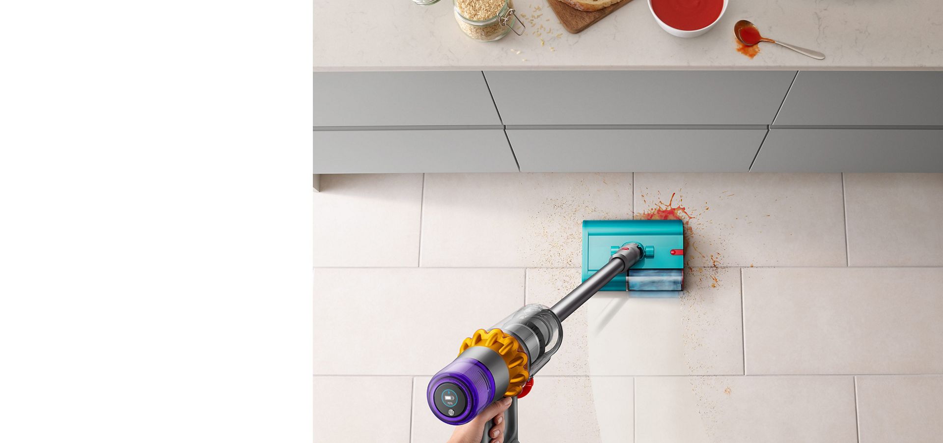 Dyson V15s Detect Submarine wet roller head clearing up spilt soup and breadcrumbs on a tiled kitchen floor near a countertop.