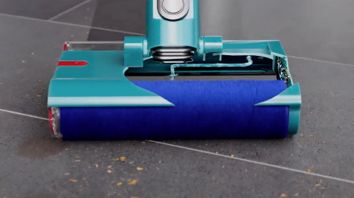 Dyson Submarine wet roller head approaches debris and liquids on a stone floor leaving behind a clean sheen.