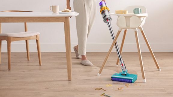 Dyson vacuum picks up debris from hard floor. A baby seat is in background. 