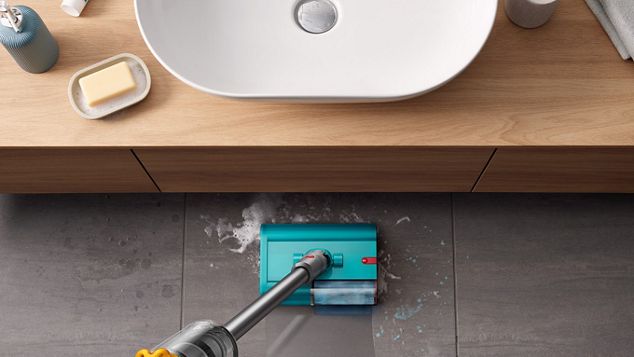 Dyson V15s Detect Submarine Wet roller-mundstykket rengør sæbevand og tandpasta på et flisebelagt badeværelsesgulv med et bassin placeret i forbilledet.