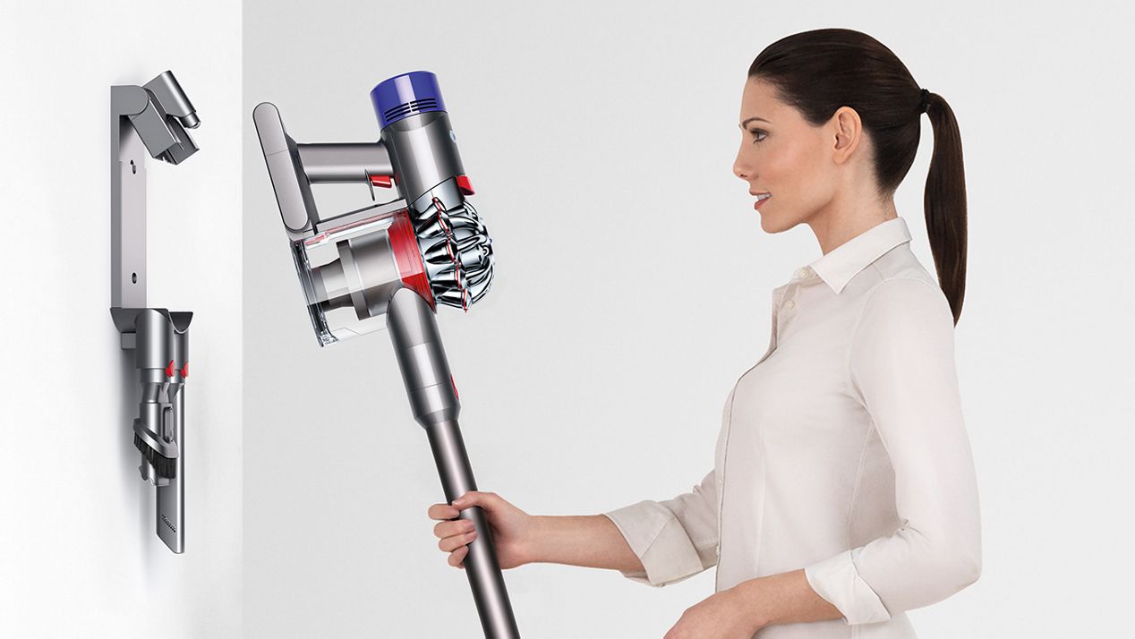 Une femme plaçant l’aspirateur Dyson V8 sur sa station de charge