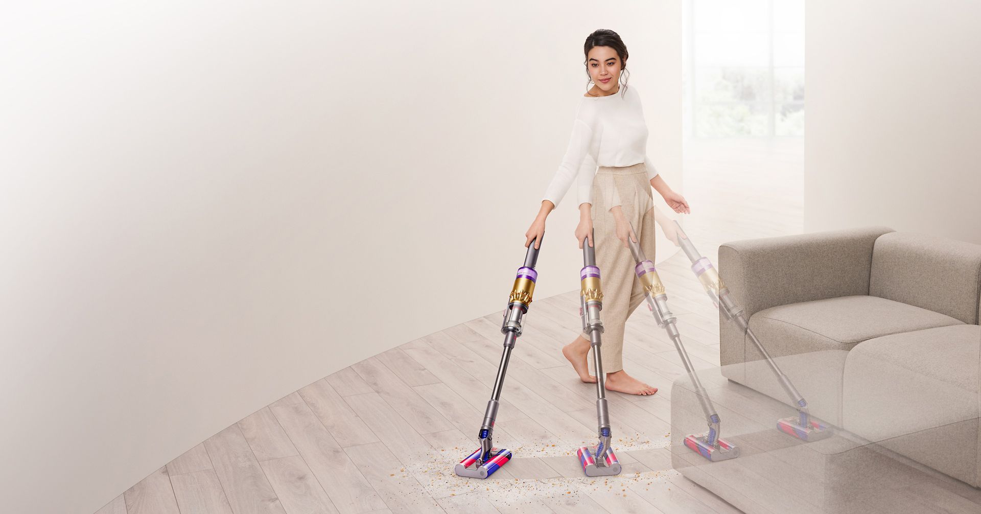 Dyson Omni-glideクリーナーでソファー周りの床を掃除する女性。