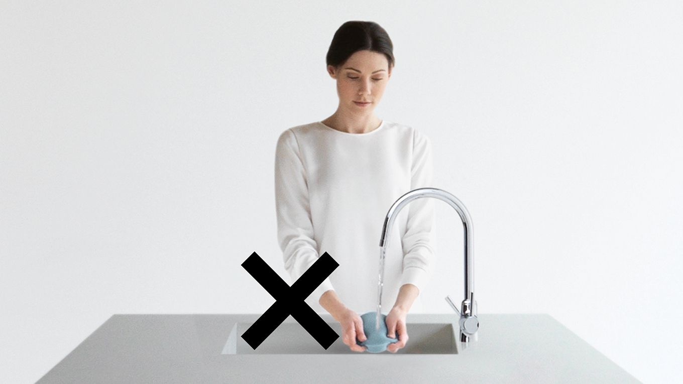 Image d'une femme en train de laver le filtre d’un aspirateur dans son évier, barrée d’une croix. Image d'une femme en train de laver le filtre d’un aspirateur dans son évier, barrée d’une croix.