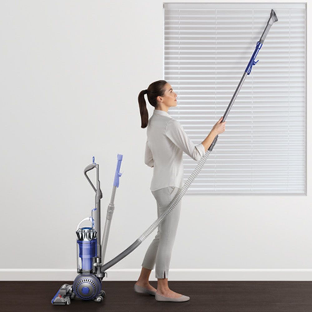 A Dyson upright vacuum with extended long reach tool cleaning a blind.
