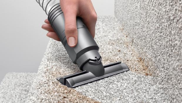 Upright vacuum cleaner being steered in a sweeping arc across a black hard floor surface.