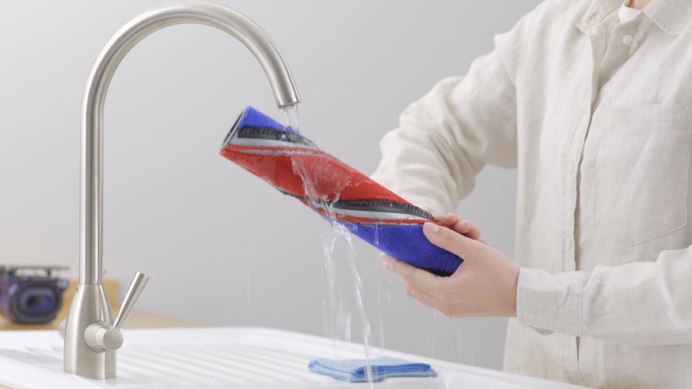 An owner washes their Dyson 360 Vis Nav’s brush bar under running water.