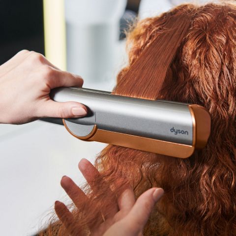 Primo piano della piastra Dyson Airstrait che liscia lunghi capelli neri.