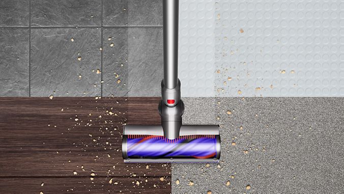 Vue du dessus de l’aspirateur Dyson V8 nettoyant des débris sur un sol dur et de la moquette.