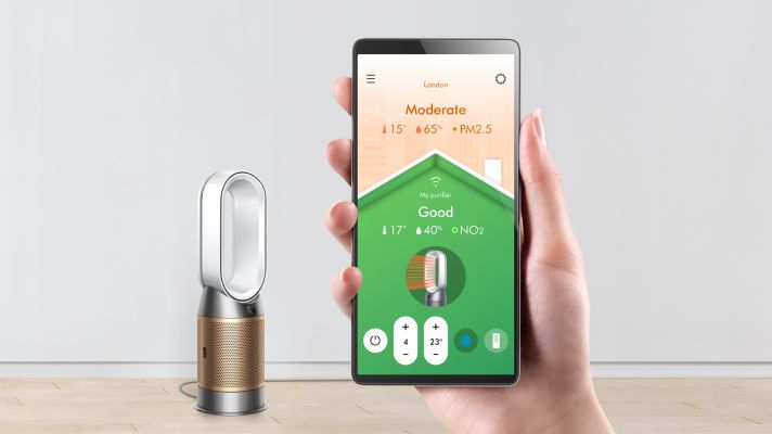A hand holding a smartphone showing the air quality screen, with the Dyson Purifier Hot+Cool Formaldehyde.