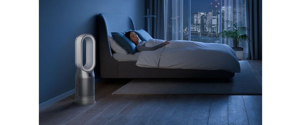 The Dyson Purifier Humidify+Cool Autoreact in a dark bedroom at night as a woman sleeps in her bed.