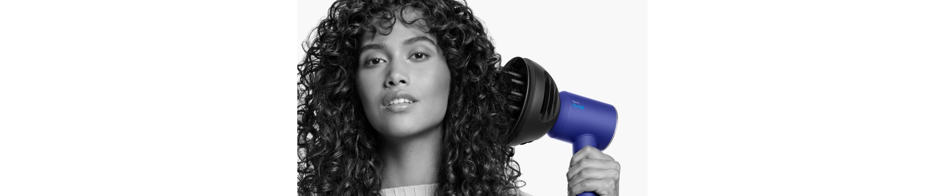 Close up of a woman adding volume to her curly hair with the Dyson Wave+Curl diffuser