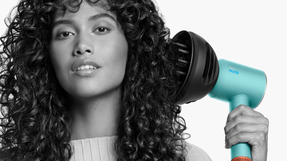 Nahaufnahme einer Frau, die ihrem lockigen Haar mit dem Dyson Wave+Curl Diffusor Volumen verleiht