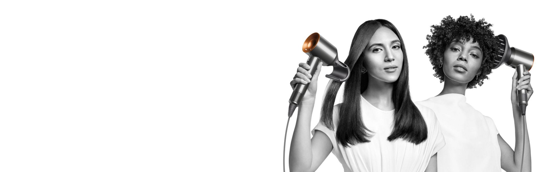 Zwei Frauen trocknen ihr Haar mit dem Dyson Supersonic Haartrockner. Die Frau links nutzt den Aufsatz zur Bändigung fliegender Haare, um ihr glattes langes Haar zu glätten, und die Frau rechts nutzt den Diffusor-Aufsatz, um ihr krauses kurzes Haar zu formen. 
