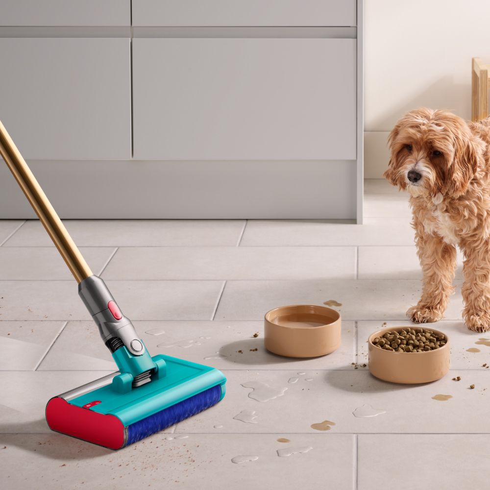 The Dyson V15s Detect Submarine cleans the floor of a kitchen with a dog and dog food bowls in the background.