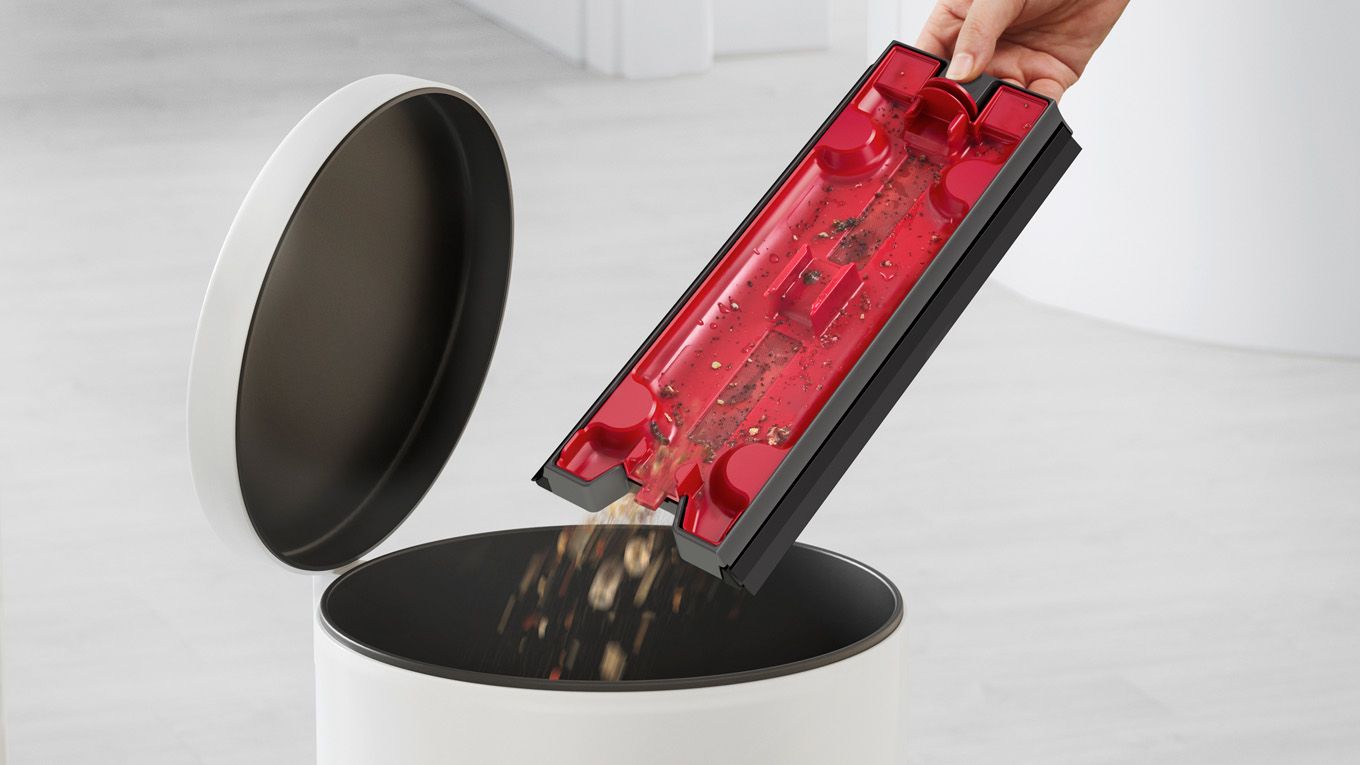 Emptying the debris tray into a bin.