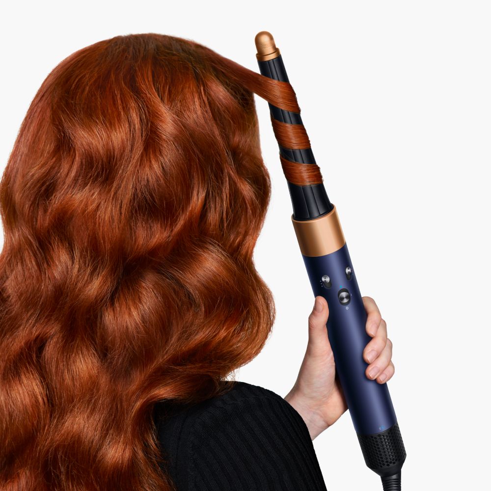A redhead model uses the Dyson Airwrap i.d. curl feature to curl her hair.