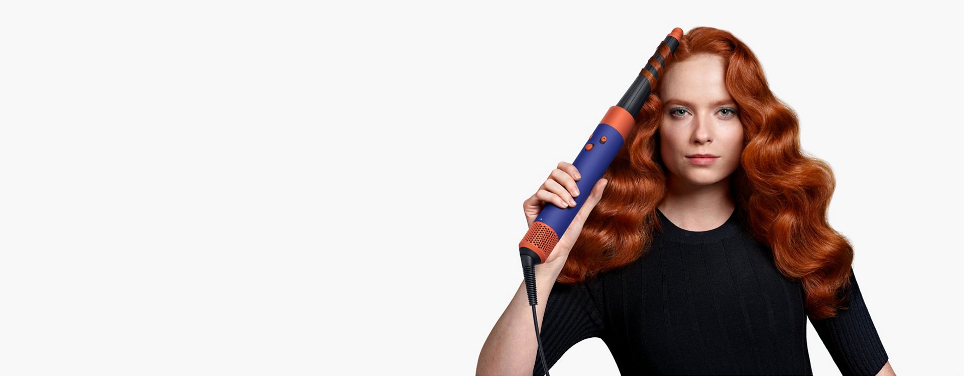 Ein Model mit langem, gewelltem rotem Haar kreiert Wellen mit dem Dyson Airwrap i.d. Multi-Styler und -Trockner