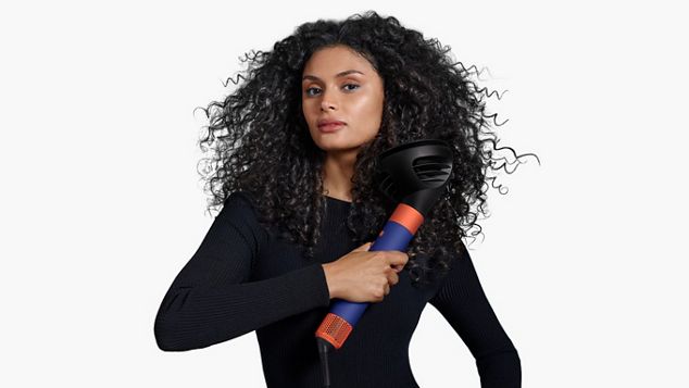 Modell med teksturerte krøller holder en Dyson Airwrap i.d.