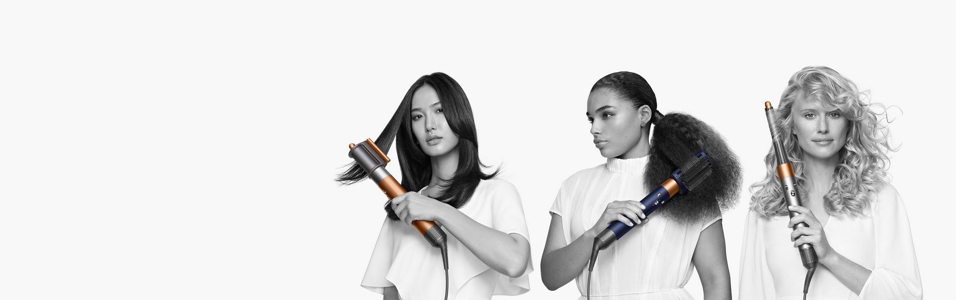 Three models each holding a Dyson Airwrap multi-styler. One model with the Coanda smoothing dryer attachment, one with the Firm smoothing brush and 30mm long barrel. 