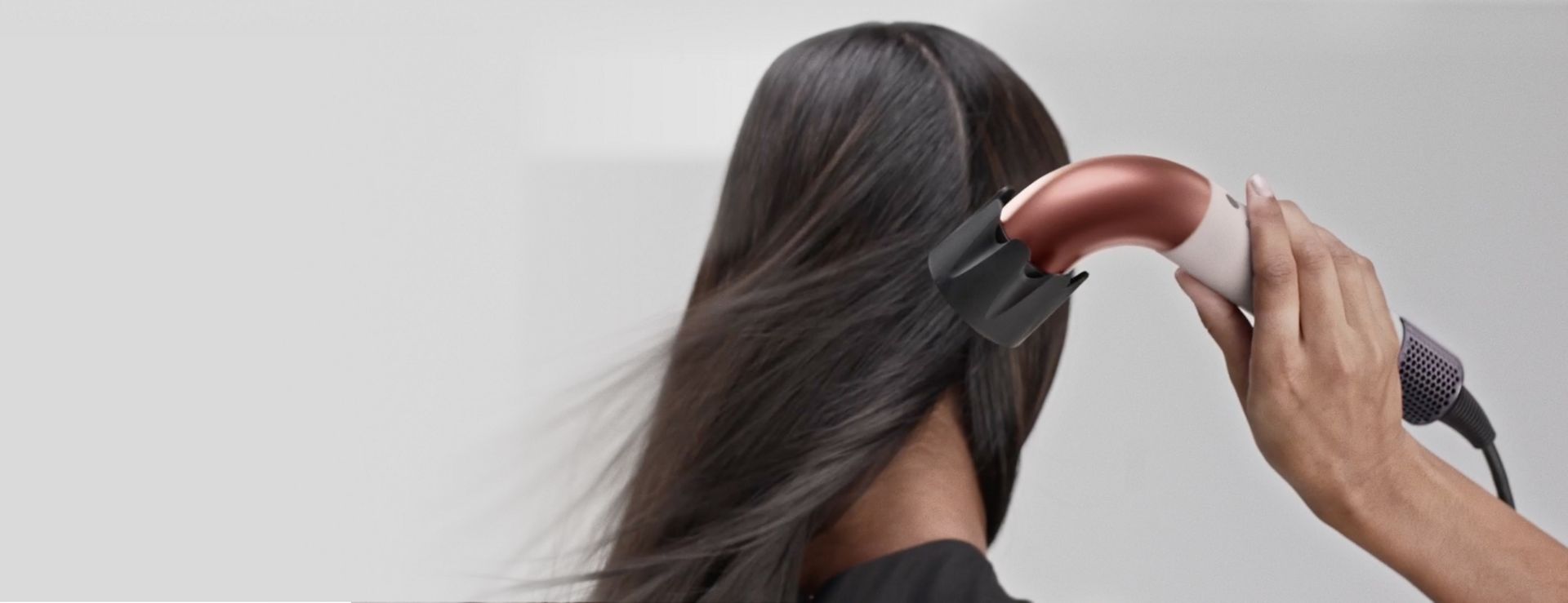 Uma modelo seca o cabelo com o secador de cabelo Dyson Supersonic r e o acessório de ar potente que gera um fluxo de ar potente.